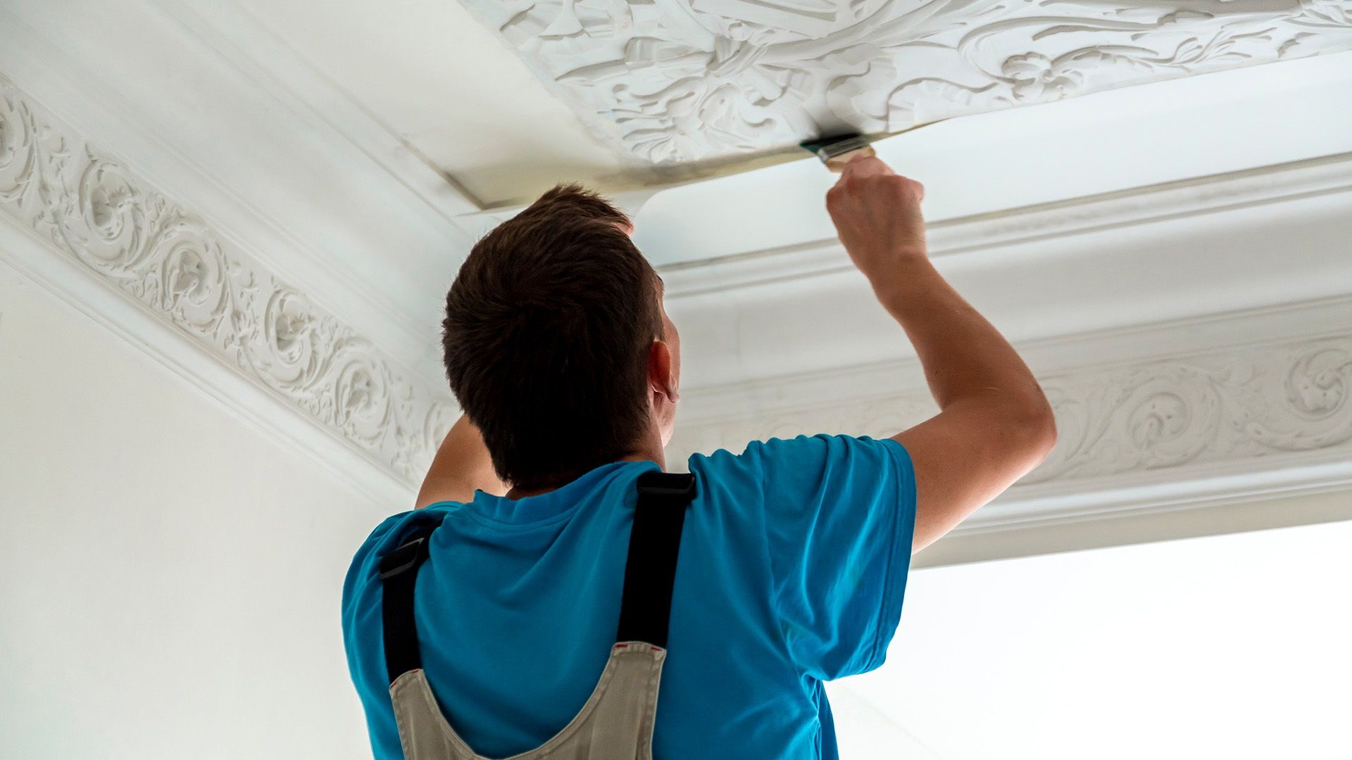 Mann arbeitet mit Pinsel an einer Wand mit Stuck